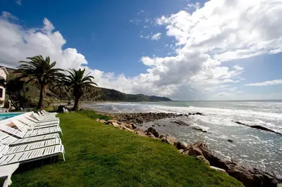 a row of white benches sitting next to the ocean at Cliff House Inn in Carpinteria
