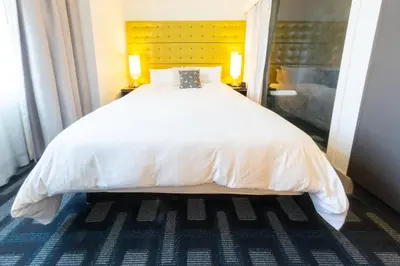 a bedroom with a large white bed with a yellow headboard at Padre Hotel in Bakersfield