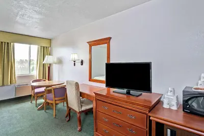 a hotel room with a desk with a television and a table at Days Inn & Suites by Wyndham Fullerton in Fullerton