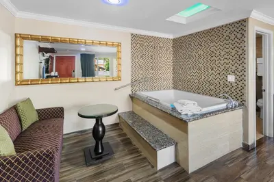 a room with a tub and a chair and a mirror at Sky Palm Motel - Orange in Orange