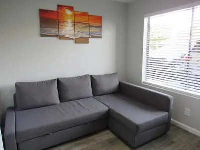 a grey couch in a room with a window at Capri Suites Anaheim in Anaheim