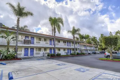 a building with blue doors and palm trees in a parking lot at Motel 6 Chino, CA - Los Angeles Ontario in Chino