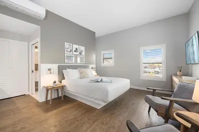 a white bedroom with a bed and a chair at Sea Sprite Beach Club in Hermosa Beach