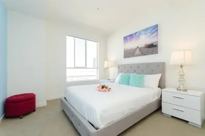 a white bedroom with a large bed and a red stool at Modern Apartment Rentals in Los Angeles