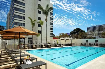 a pool with chairs and an umbrella next to a building at DoubleTree by Hilton LAX - El Segundo in El Segundo