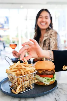 a woman sitting at a table with a hamburger and french fries at Andaz West Hollywood, By Hyatt in Los Angeles