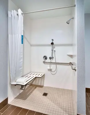 a white bathroom with a shower and a bench at Hampton Inn & Suites Anaheim Resort Convention Center in Anaheim