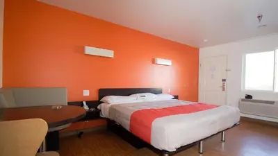 a bedroom with an orange wall with a bed and a table at Motel 6 Victorville in Victorville