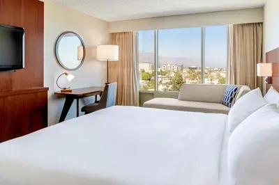 a hotel room with a bed and a desk and a window at Hilton Pasadena in Pasadena