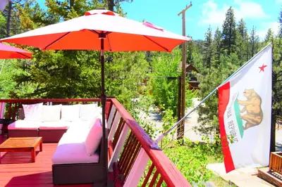 a deck with an umbrella and couches and a table at Dream Getaway-Secluded Hot Spa-Walk to Village-Walk to Pineknot Trailhead-Plus King Bed! in Big Bear Lake