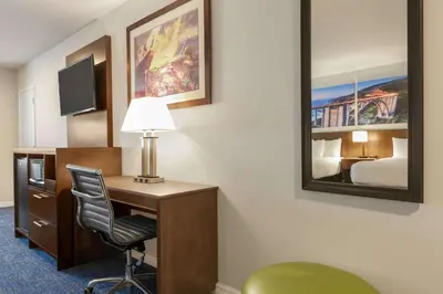 a hotel room with a desk and a bed and a mirror at Days Inn & Suites by Wyndham Anaheim At Disneyland Park in Anaheim