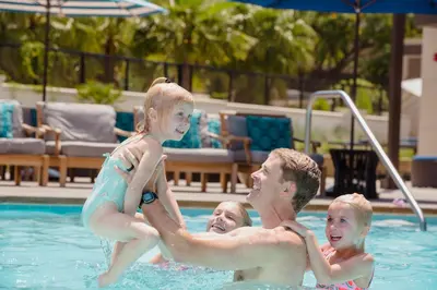 a man and two children playing in a swimming pool at Anaheim Resort Suites in Anaheim