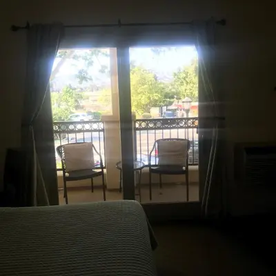 a bedroom with a bed and a balcony with two chairs at Bella Capri Inn and Suites in Camarillo