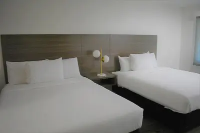 two beds in a hotel room with white sheets at Signature Anaheim Maingate in Anaheim