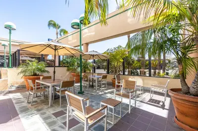 a patio with tables and chairs and palm trees at New Gardena Hotel in Gardena