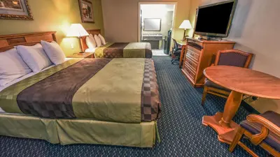 a hotel room with two beds and a table and a television at Chariot Inn Glendale - Pasadena in Glendale