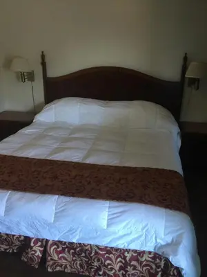 a large bed with white sheets and a wooden headboard at Frontier Motel in Anaheim