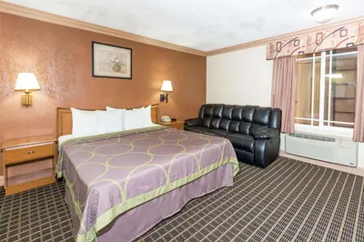a hotel room with a bed and a leather chair at Super 8 by Wyndham Azusa in Azusa
