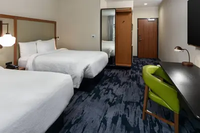 a hotel room with two beds and a green chair at Fairfield Inn & Suites by Marriott Moorpark Ventura County in Moorpark