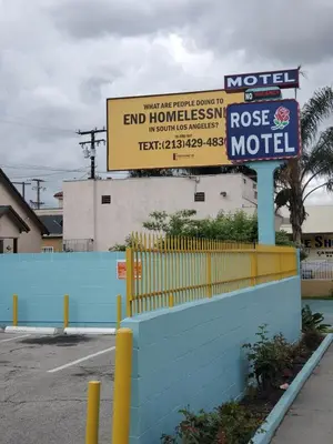 a motel sign in a parking lot next to a fence at Rose motel in Compton
