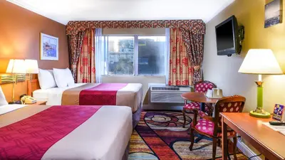 a hotel room with two beds and a desk at Vagabond Inn Long Beach in Long Beach