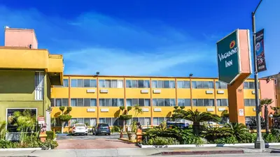 a yellow building with cars parked in a parking lot at Vagabond Inn Long Beach in Long Beach