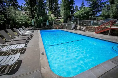a large blue swimming pool with lounge chairs around it at Lakeside Family Cabin by Big Bear Vacations in Big Bear Lake