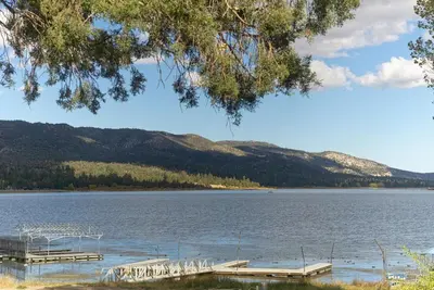 a lake with a dock and mountains in the background at Lake Shore Family Cabin w Hot Tub and Pool Table by Big Bear Vacations in Big Bear Lake