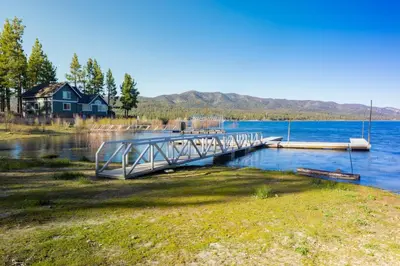 a dock on a lake with a house in the background at Lake Shore Family Cabin w Hot Tub and Pool Table by Big Bear Vacations in Big Bear Lake