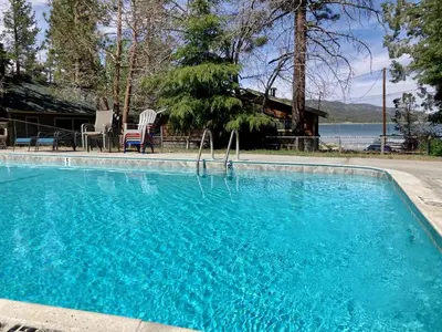 a large blue swimming pool with two chairs and a house at Lake Shore Family Cabin w Hot Tub and Pool Table by Big Bear Vacations in Big Bear Lake