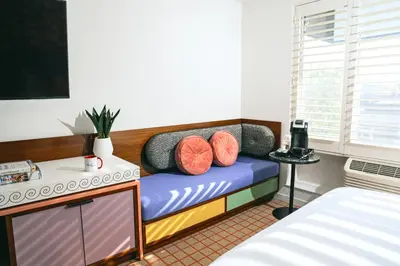 a room with two beds and a bench with pillows at The Hollywood Franklin Hotel near Universal Studios in Los Angeles