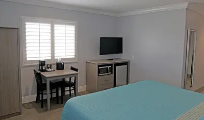 a bedroom with a bed and a desk with a television at Surf City Inn in Huntington Beach