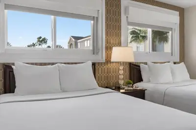 two beds in a hotel room with two windows at Peacock Suites in Anaheim