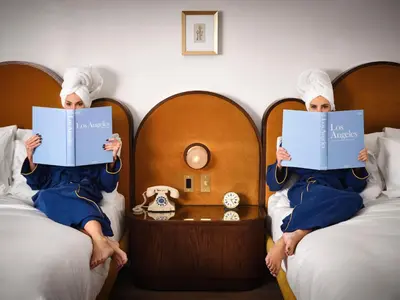 a person sitting between two beds reading books at The Georgian Hotel in Los Angeles