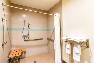 a bathroom with a shower and a bench in it at Rodeway Inn Artesia Cerritos in Artesia