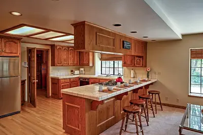 a kitchen with wooden cabinets and a kitchen island with bar stools at Lake Arrowhead House with Lake Views and Wet Bar! in Lake Arrowhead