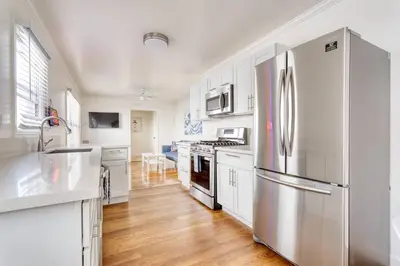 a kitchen with white cabinets and a stainless steel refrigerator at New Beach Jewel Bungalow in Long Beach