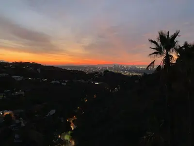 a sunset with a palm tree and a city at HOLLYWOOD HILLS JETLINER VIEWS at STUDIO 1080 HOLLYWOOD in Los Angeles
