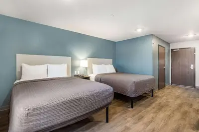 two beds in a room with blue walls and wooden floors at WoodSpring Suites Colton in Colton