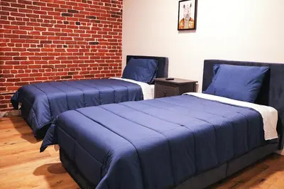 two beds with blue covers in a room with a brick wall at The Haas, Trademark Collection by Wyndham in Los Angeles