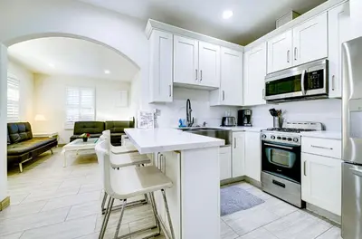 a kitchen with white cabinets and a living room at Stylish Modern Home, AC, Parking & Near FWYs in Santa Ana