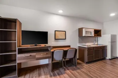 a room with a desk with a television and a kitchen at WoodSpring Suites Bakersfield Airport in Bakersfield