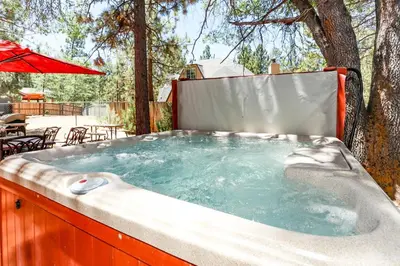 a jacuzzi tub in a backyard with a table and umbrella at Mountain Adventure - 1931 by Big Bear Vacations in Big Bear Lake