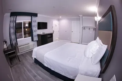 a bedroom with a large white bed and a kitchen at Travelodge Inn & Suites by Wyndham West Covina in West Covina