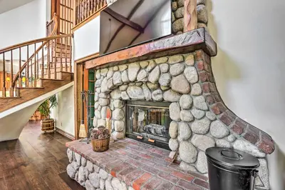 a stone fireplace in a living room with a staircase at Ornate Lake Arrowhead Home with Deck in Lake Arrowhead