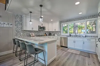 a kitchen with white cabinets and a large island with bar stools at Airy Alpine Getaway with Lake Arrowhead Views! in Lake Arrowhead