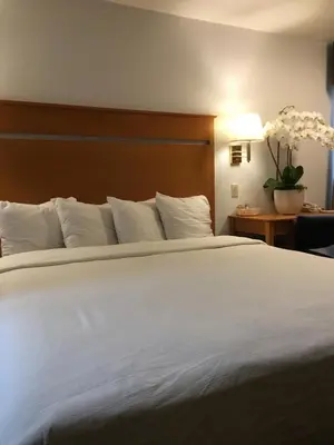 a large bed with white sheets and a wooden headboard at OceanView Motel in Huntington Beach