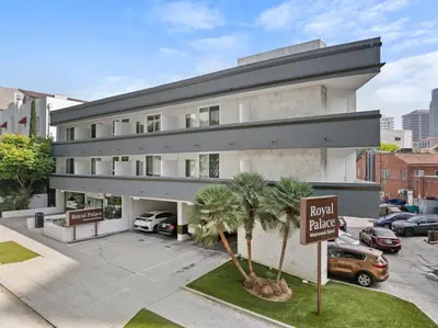 a large white building with palm trees in front of it at Royal Palace Westwood Hotel in Los Angeles