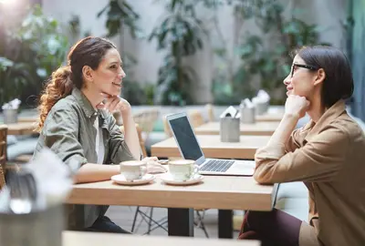 two women sitting at a table with a laptop at Studio 6 Artesia CA in Artesia