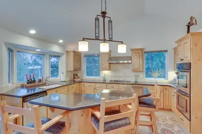 a large kitchen with wooden cabinets and a table and chairs at Beautiful Lake Arrowhead Cabin with EV Charger in Lake Arrowhead